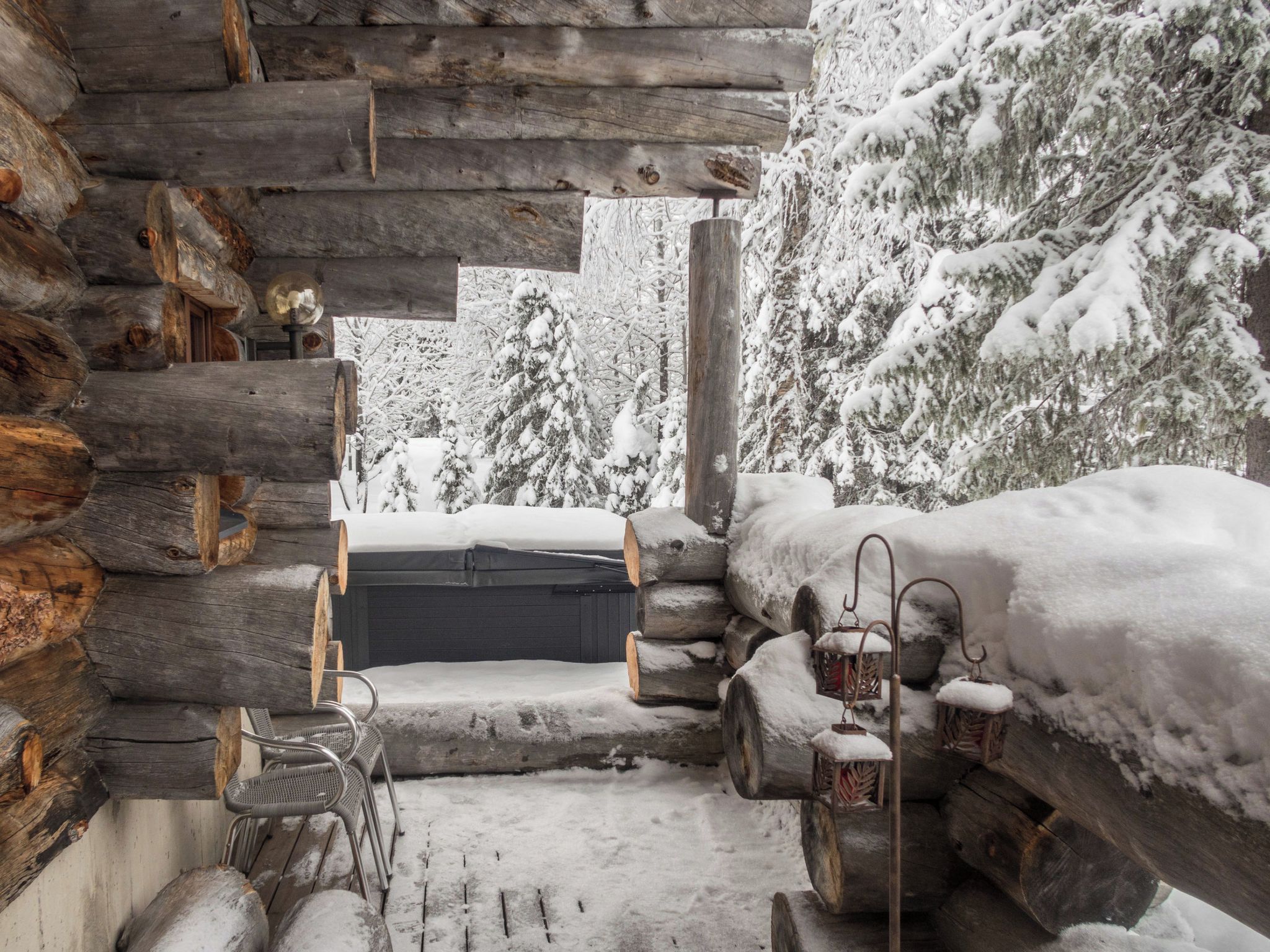Una cabaña de troncos con un jacuzzi, sillas de mimbre y faroles.