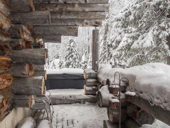 A log cabin with a hot tub, wicker chairs, and lanterns.