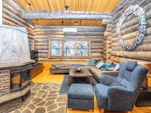 A log cabin interior with a stone fireplace, a sofa, a blue armchair, and a large window with a star decoration.