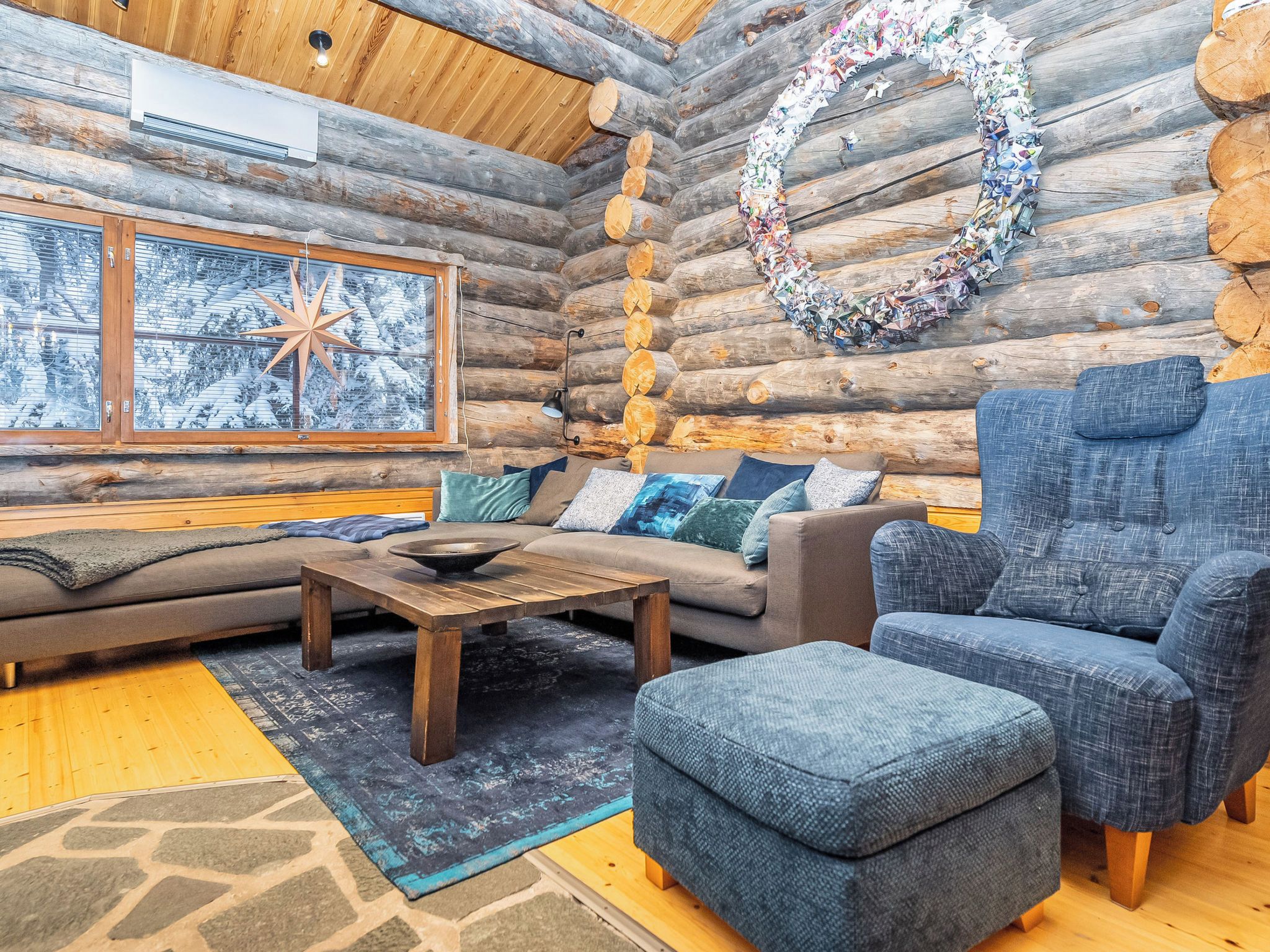 A log cabin interior with a sofa, armchair, coffee table, and a decorative wreath on the wall.