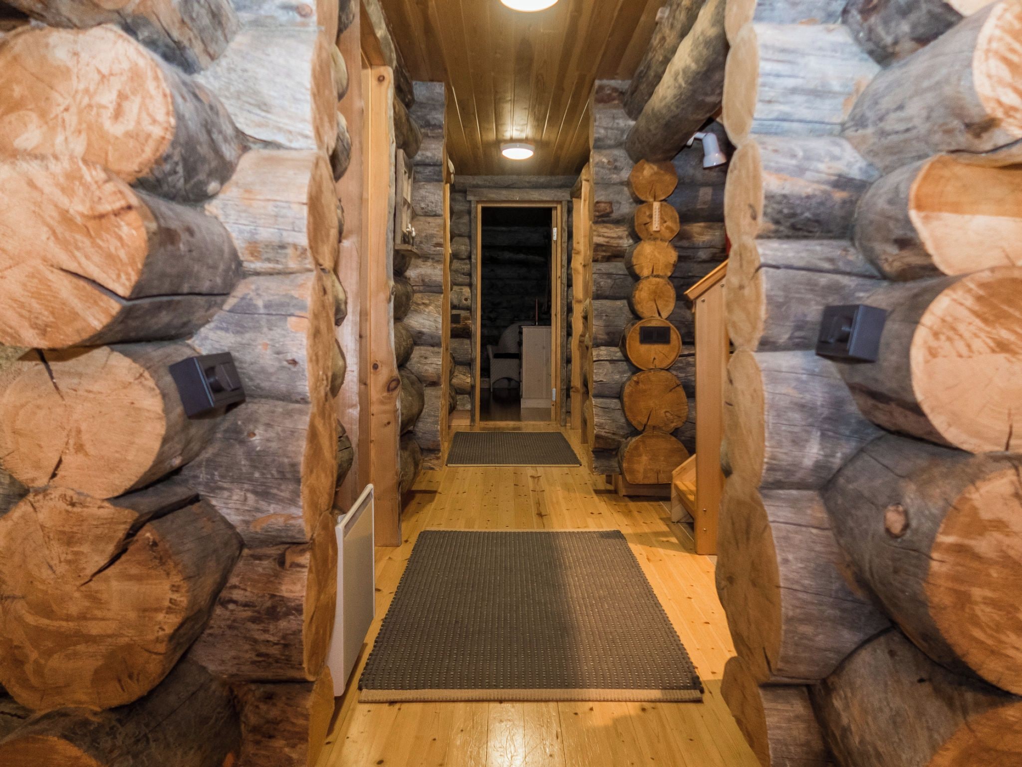 A log cabin interior with a central wooden door leading to a room, surrounded by stacked logs.