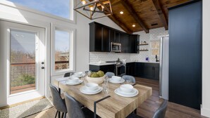 Una cucina moderna con mobili neri, un tavolo da pranzo in legno imbandito per quattro persone e un'ampia finestra con vista sulla città.