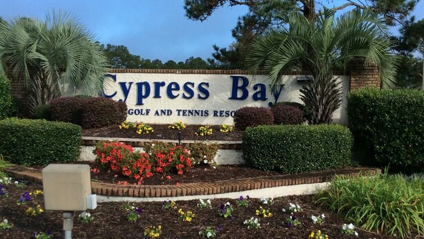 A sign for Cypress Bay Golf and Tennis Resort with a landscaped garden in front.