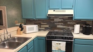 A kitchen with teal cabinets, a white microwave, a black stove, and a stainless steel sink.
