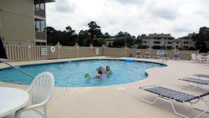 A swimming pool area with a wooden fence, lounge chairs, and a pool table.