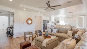 A spacious living room with a beige sofa, a coffee table, and a dining area with a small table and chairs. A kitchen is visible in the background with modern appliances. - Destination Ledges Utah (St. George)