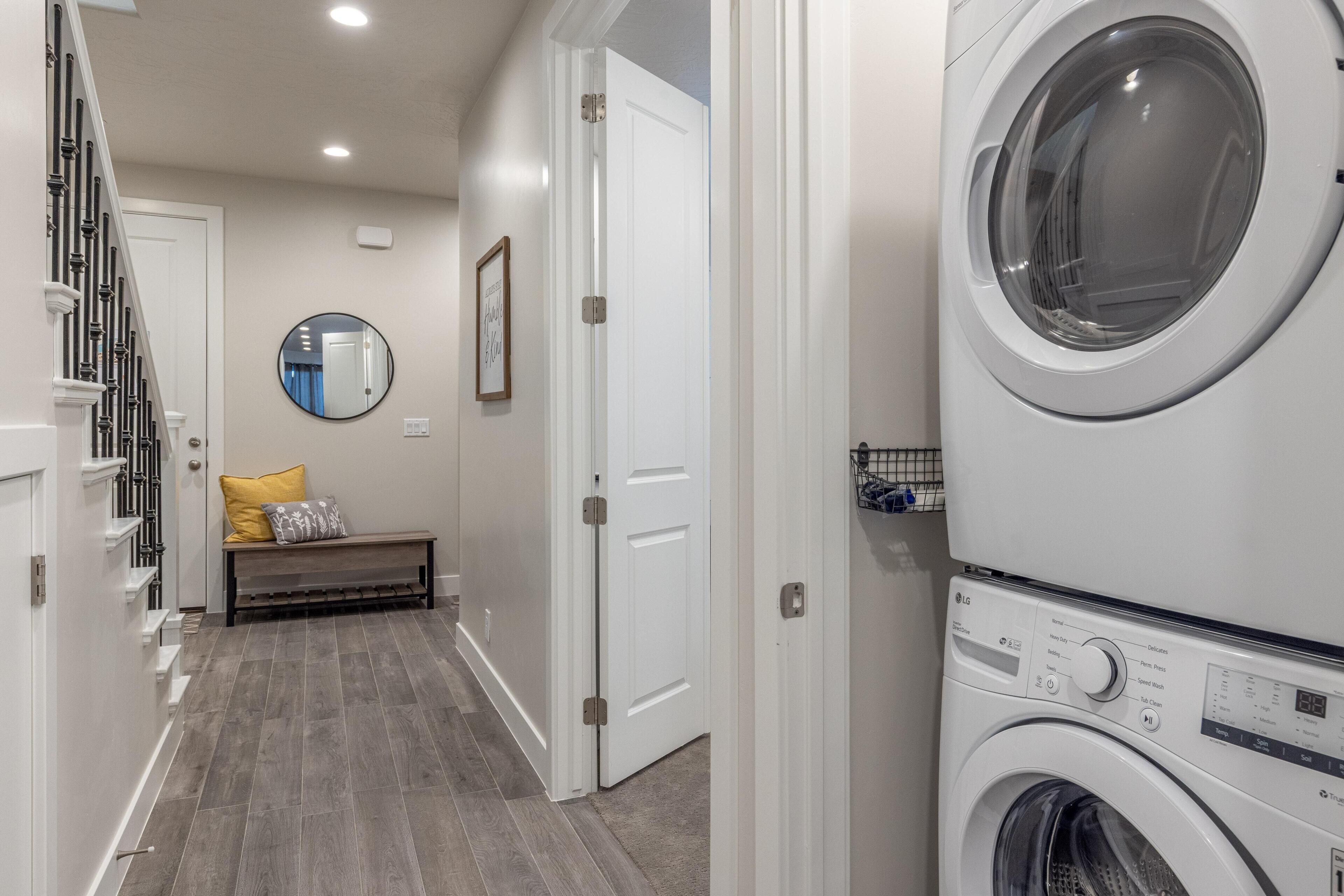 A laundry room with stacked washers and dryers, a bench with pillows, a mirror, and a door leading to another room.