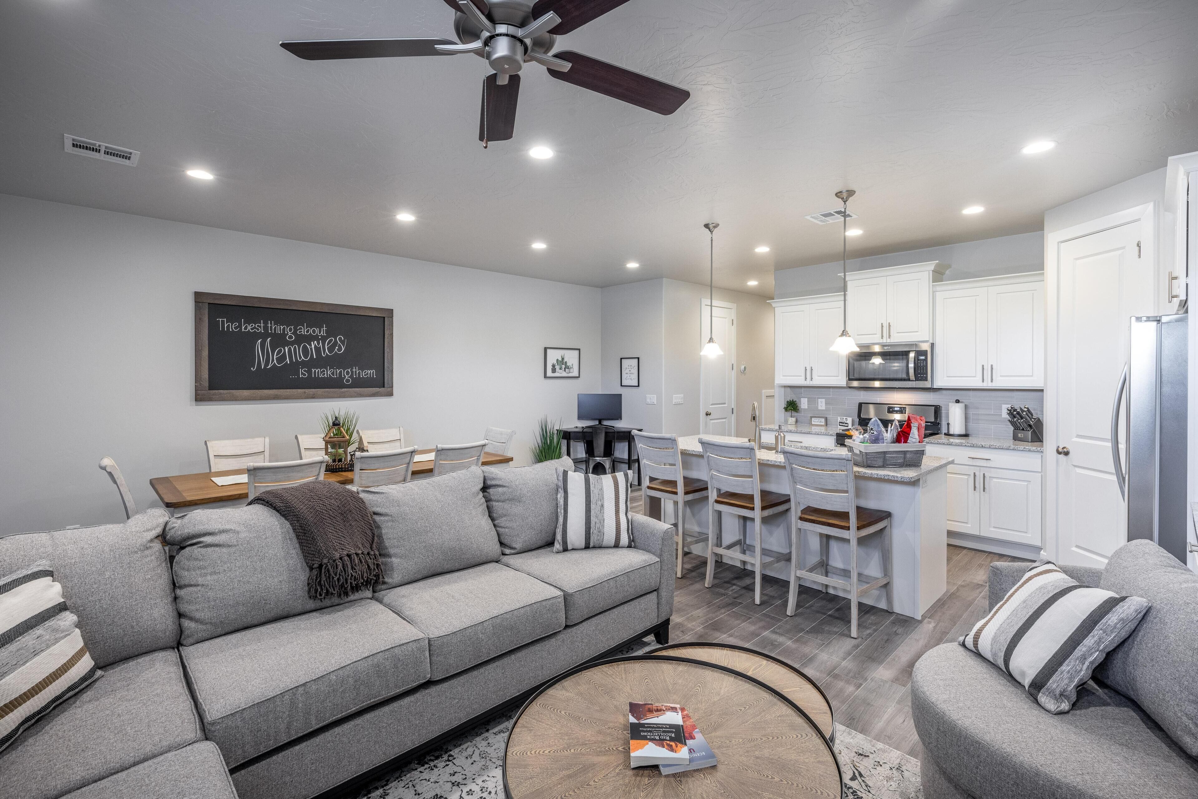 A modern living room with a grey sofa, a coffee table, and a dining area with white chairs and a kitchen in the background.