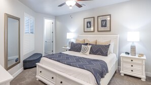 Une chambre à coucher comprenant un lit, des tables de chevet, une commode, un ventilateur de plafond et une porte.