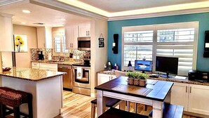 A modern kitchen with a central island, wooden flooring, and a view through large windows. - Steps from Beach, Gorgeous Sunset Views, Recently Renovated, 2BD/2BTH, Sleeps 4 (Fort Myers Beach)