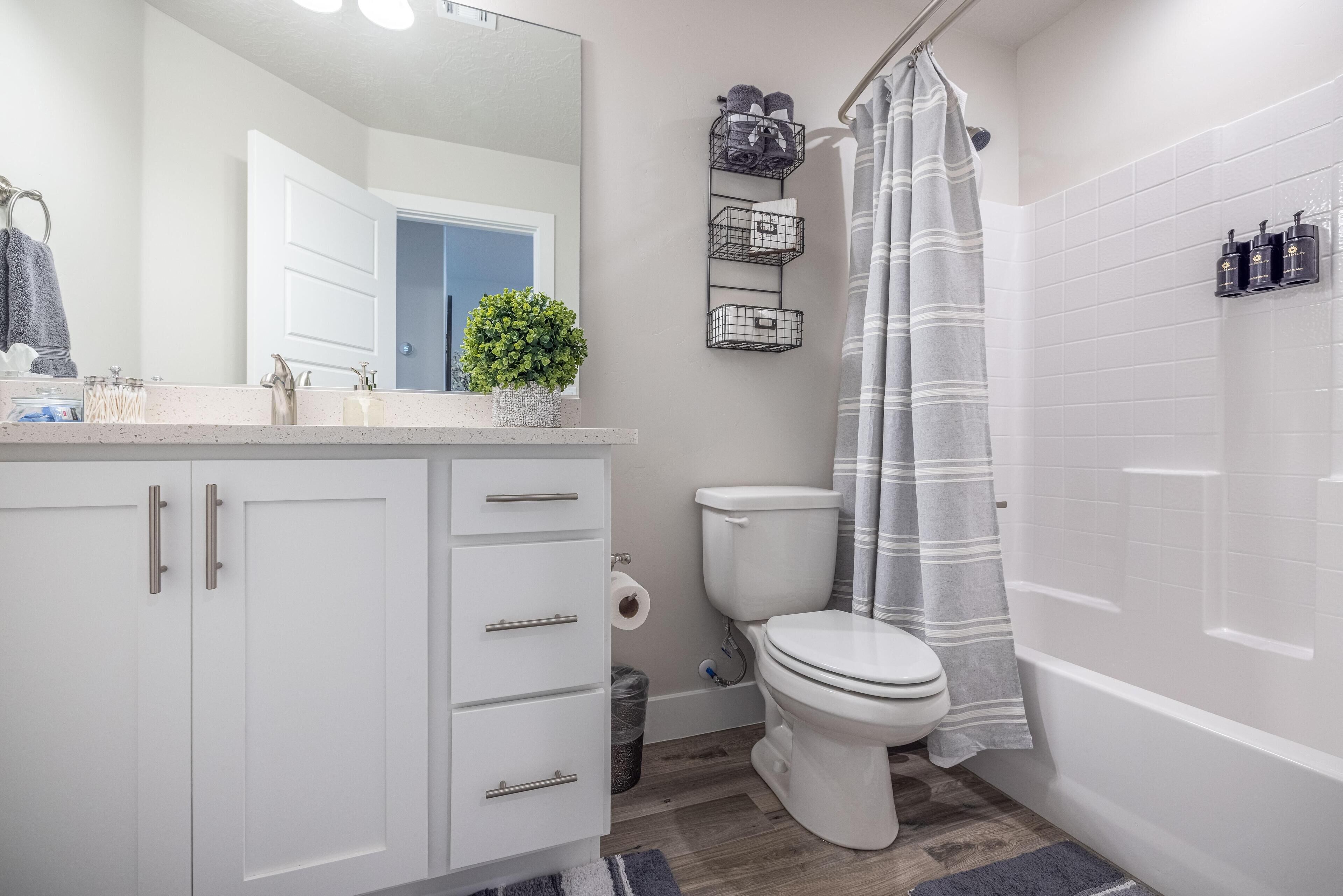 Une salle de bain moderne avec un meuble-lavabo blanc, des toilettes, une douche avec un rideau à rayures et une petite étagère contenant des articles de toilette.