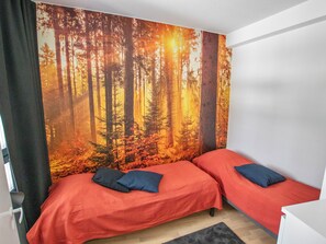A bedroom with two beds, a forest mural on the wall, and a window with curtains. - Ylälänsi 3 as 9 by Interhome (Ylläsjärvi)
