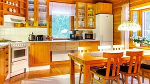 A wooden cabin-style kitchen with a dining area, wooden cabinets, a refrigerator, a stove, and a hanging light fixture. - Riekkotupa by Interhome (Enontekiö)