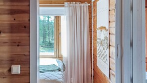 A wooden cabin bedroom with a bed, a window with curtains, and a wall with a decorative panel. - Riekkotupa by Interhome (Enontekiö)