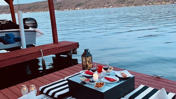 Una terrassa de fusta amb taula preparada per a dinar, amb vista a un llac tranquil.