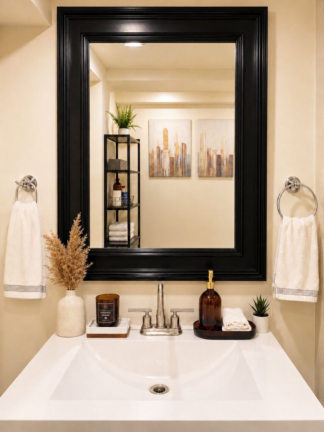 A bathroom with a large mirror, a white sink, a black shelf with toiletries, and two towels hanging on towel rings.