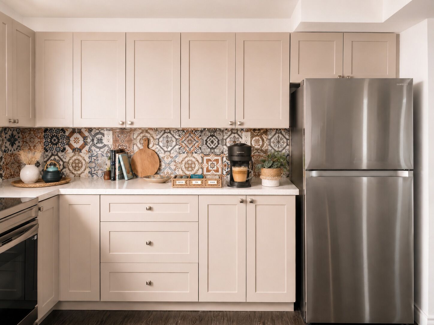 A kitchen with light-colored cabinets, a stainless steel refrigerator, a coffee maker, and a patterned backsplash.