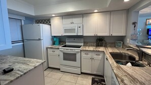 A modern kitchen with white cabinets, a built-in oven, microwave, and a sink. - Amazing Beachfront Condo (Jensen Beach)