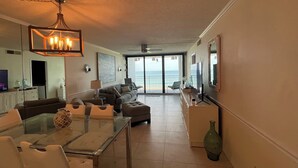 A spacious living room with a glass coffee table, sofas, and a TV. A balcony with a view of the ocean is visible. - Amazing Beachfront Condo (Jensen Beach)