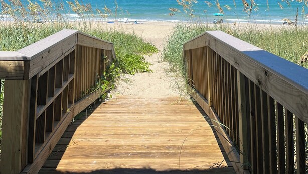 A wooden pathway leading to a beach with a thatched roof overhead. - Amazing Beachfront Condo (Jensen Beach)