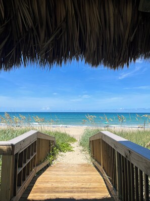 A wooden pathway leading to a beach with a thatched roof overhead. - Amazing Beachfront Condo (Jensen Beach)