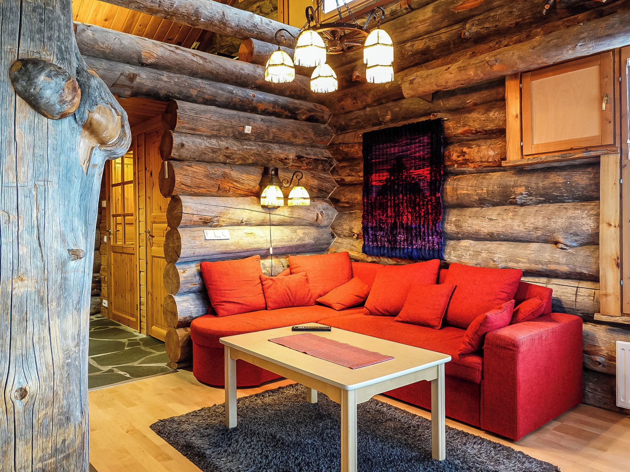 A log cabin interior with a red sofa, a small table, and a chandelier.