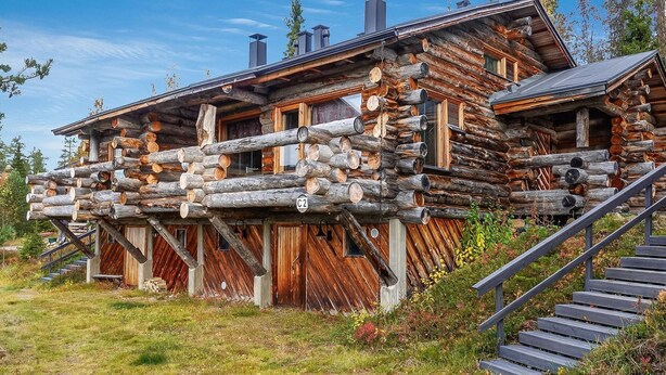 En træhytte med en træterrasse og en trappe op til indgangen.