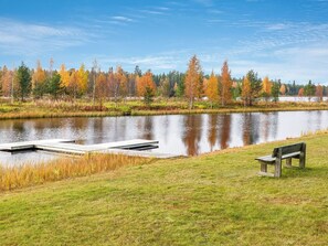 A calm lake with a dock and a bench, surrounded by trees with autumn foliage.