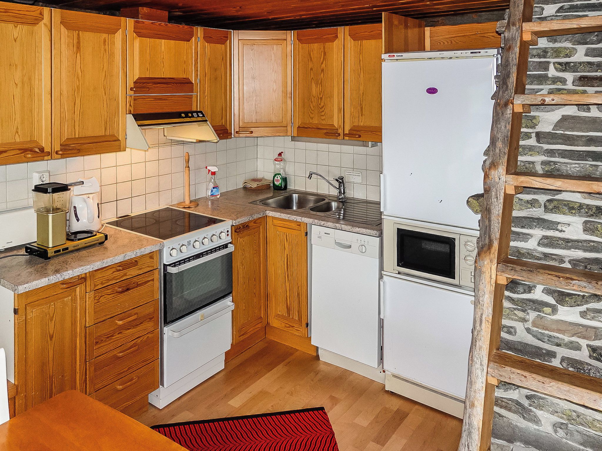 Una cocina con armarios de madera, un refrigerador blanco, una estufa, un lavamanos y una pared de piedra.