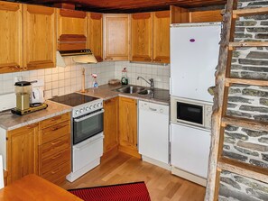 A kitchen with wooden cabinets, a white refrigerator, a stove, a sink, and a stone wall. - Sallanhelmi c2 by Interhome (Salla)