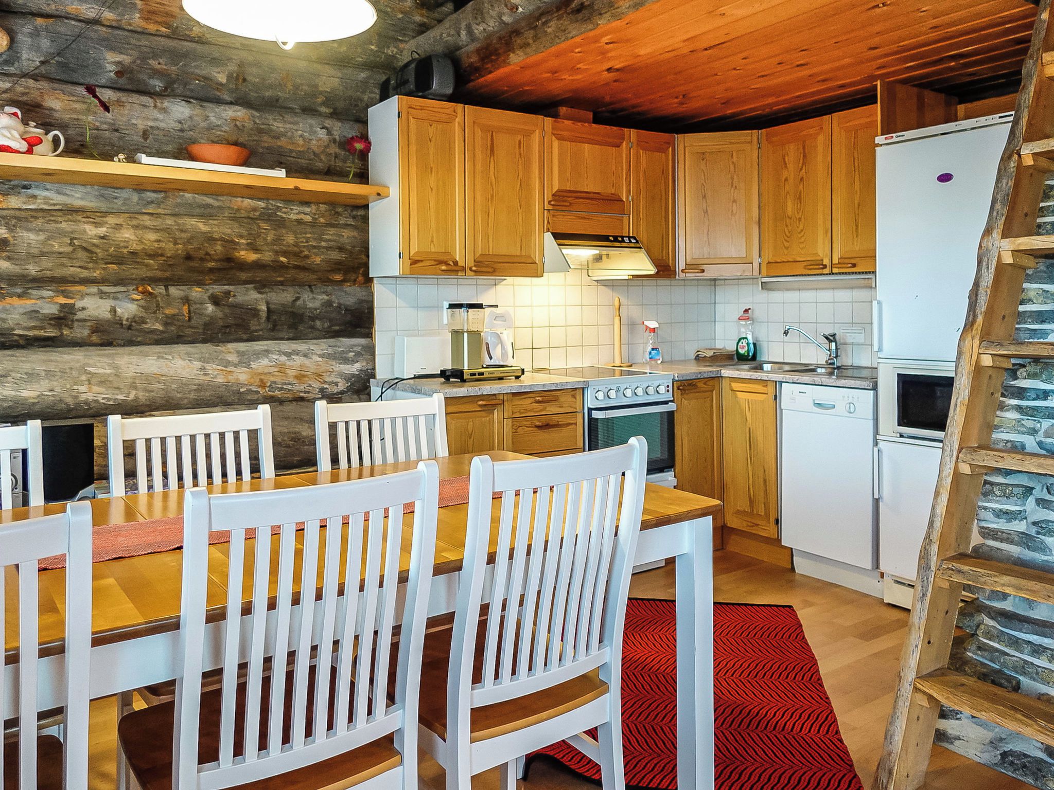 A rustic kitchen with wooden cabinets, a dining table with chairs, a stove, and a refrigerator.