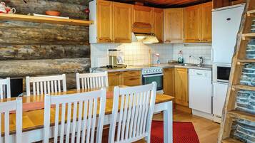 A rustic kitchen with wooden cabinets, a dining table with chairs, a stove, and a refrigerator.