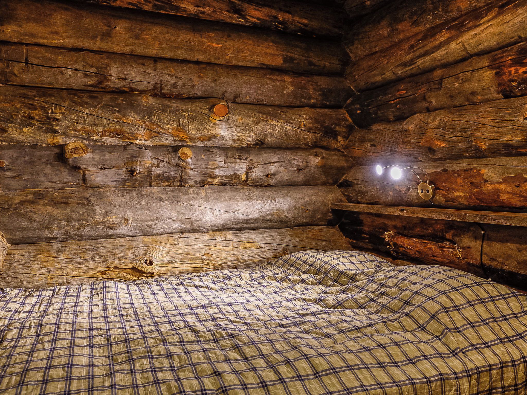 A log cabin interior with a bed and a single light source.