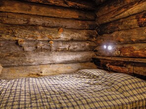 A log cabin interior with a bed and a single light source. - Sallanhelmi c2 by Interhome (Salla)