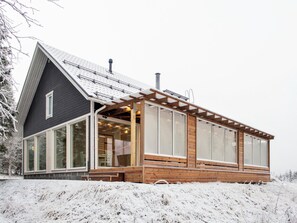 A modern house with a large glass facade, wooden deck, and a steeply pitched roof.
