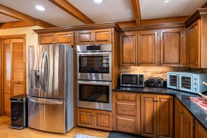 A kitchen with wooden cabinets, stainless steel appliances, a trash can, and a microwave. - Bhakti Manor Creekside Home (Franklin)