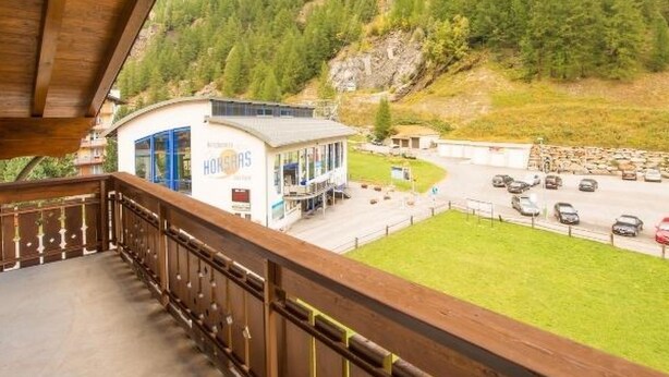 Ein Hotel mit Balkon und Blick auf einen Parkplatz sowie eine Berglandschaft.