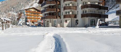 Et hotel med flere etager, altaner, en skilift og et snedækket bjerglandskab i baggrunden.