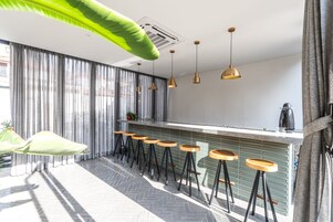 Un bar moderno con una barra larga, varios taburetes, lámparas colgantes y un amplio ventanal con cortinas.