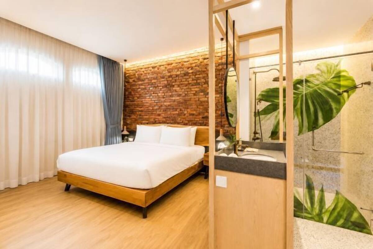 A room with a bed, a brick wall, and a shower area with a plant.