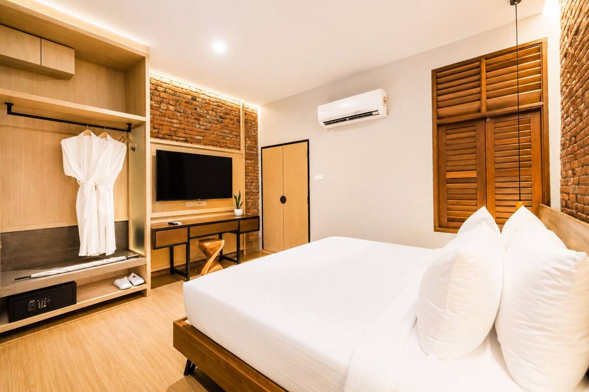 A hotel room with a bed, TV, wardrobe, desk, and an air conditioning unit.