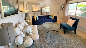 En moderne stue med sofa, lænestole, sofabord og et stort vindue.