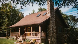 A log cabin with a stone chimney, a porch with steps, and a small deck. - 4-bedroom Vacation Cabin on 50 Private Acres (Moorefield)