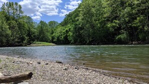 A riverbank with a rocky shore and dense greenery in the background. - 4-bedroom Vacation Cabin on 50 Private Acres (Moorefield)