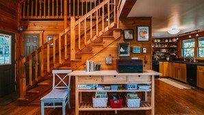 A wooden cabin interior with a wooden staircase, a kitchen area, and a bench near the door. - 4-bedroom Vacation Cabin on 50 Private Acres (Moorefield)