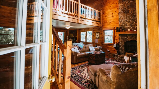 A cozy cabin interior with a loft bedroom, a fireplace, and a rustic stone wall. - 4-bedroom Vacation Cabin on 50 Private Acres (Moorefield)