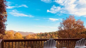 A wooden deck with Adirondack chairs and a view of autumn foliage and mountains. - 4-bedroom Vacation Cabin on 50 Private Acres (Moorefield)