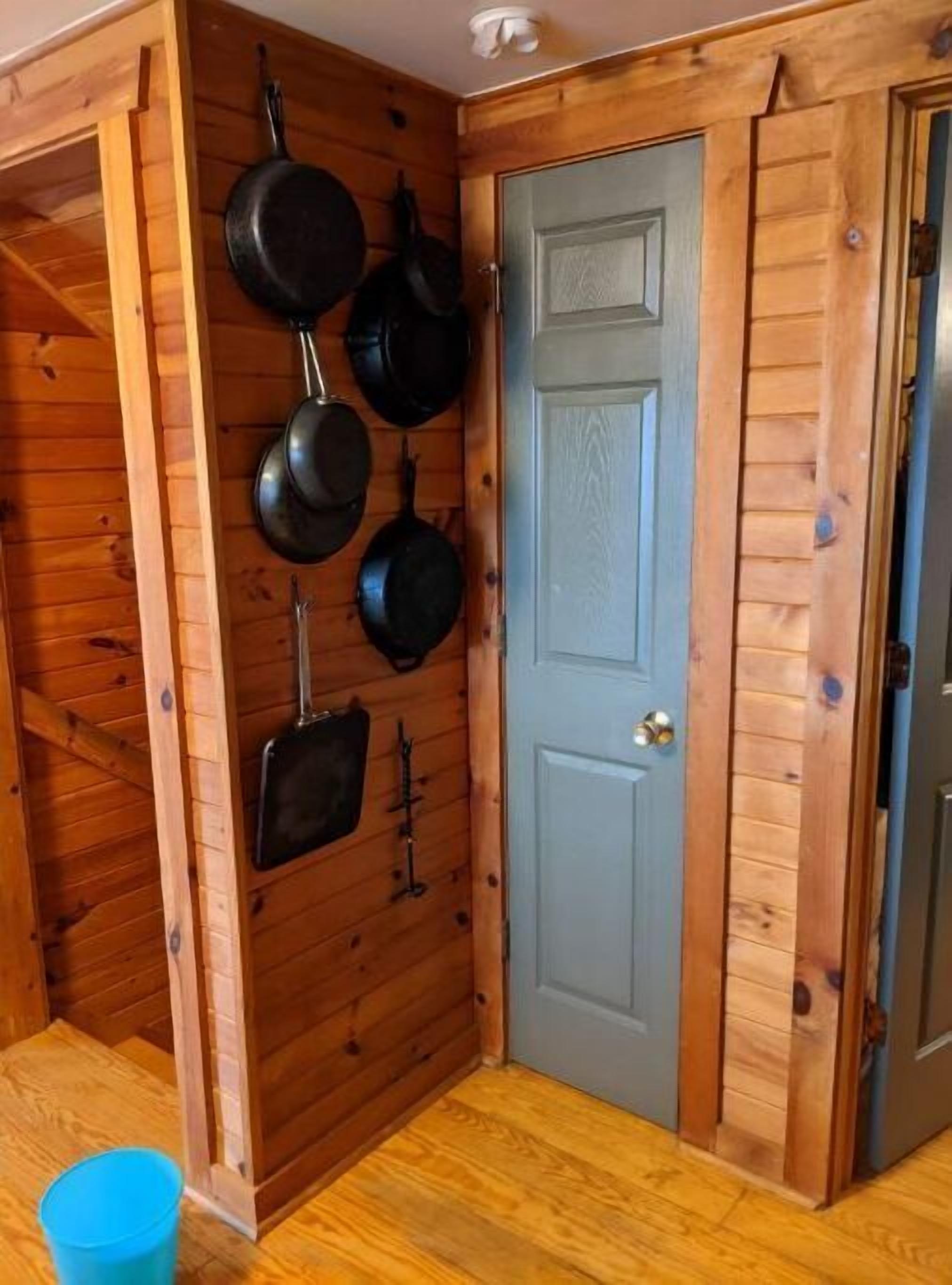 Un interior de madera con una puerta, una repisa de pared y un cubo azul en el suelo.