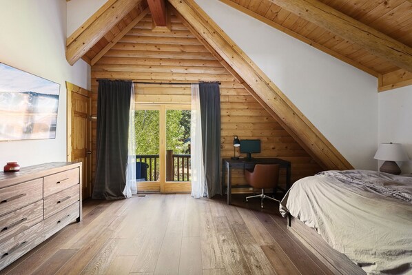 A bedroom with a sloped ceiling, wooden floor, a bed, a desk, and a chair. - Rustic Modern TRUE Log Cabin (Big Bear Lake)