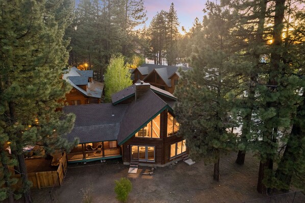 A cabin with a large deck and multiple windows, surrounded by tall pine trees.